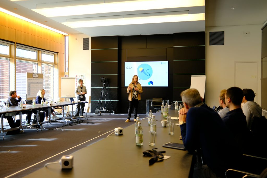 Zwei Frauen halten eine Präsentation vor einer Gruppe, die an Tischen in U-Form um sie herumsitzen