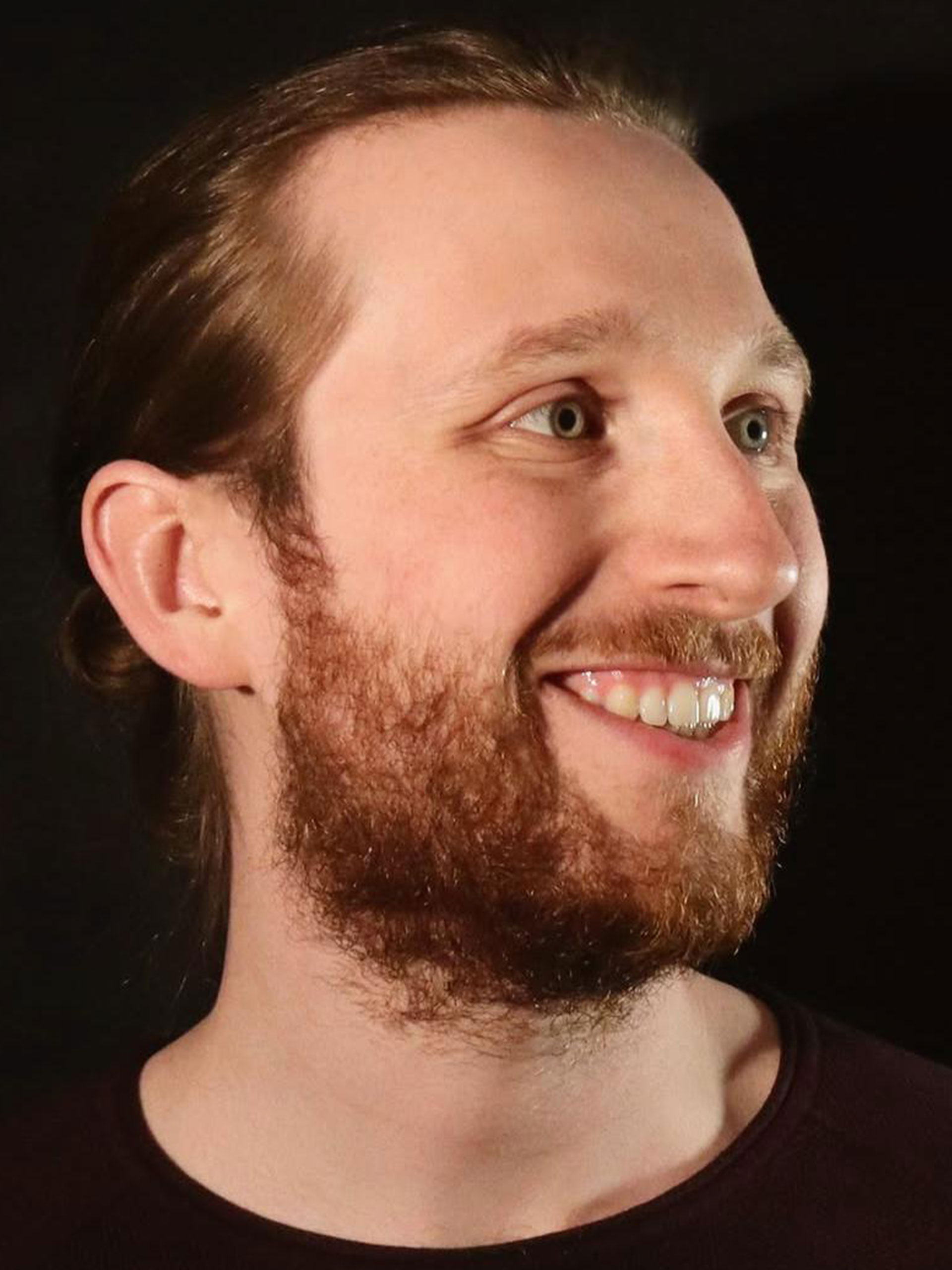 Portrait eines Mannes mit Bart im schwarzen T-Shirt vor einem schwarzen Hintergrund