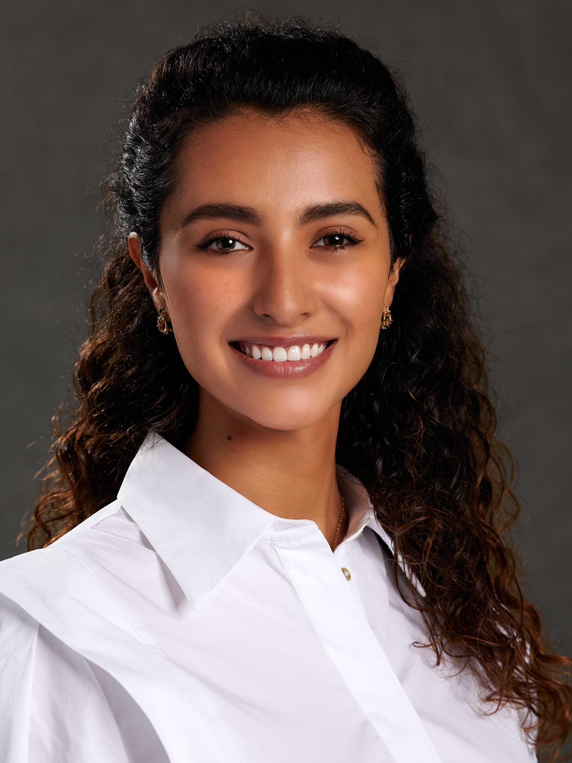 Portraitaufnahme Frau mit dunklen langen gelockten Haaren, einer weißen Bluse und einem offenen, freundlichen Lächeln