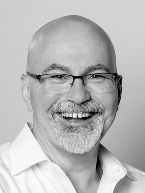 Portraitaufnahme eines Mannes mit Brille, Glatze und einem offenen, sympathischen Lächeln