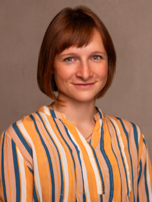 Portrait einer Frau mit mittellangem rötlichen Haar, Pony und einer gestreifter Bluse